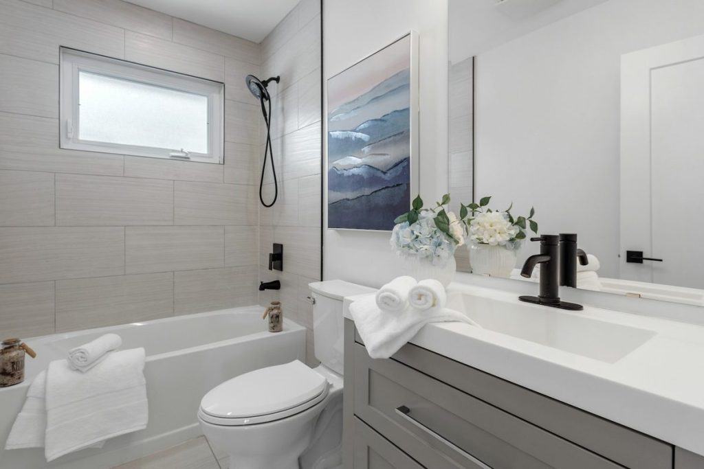Alcove bathtub with a handheld shower, folded towels and a window above
