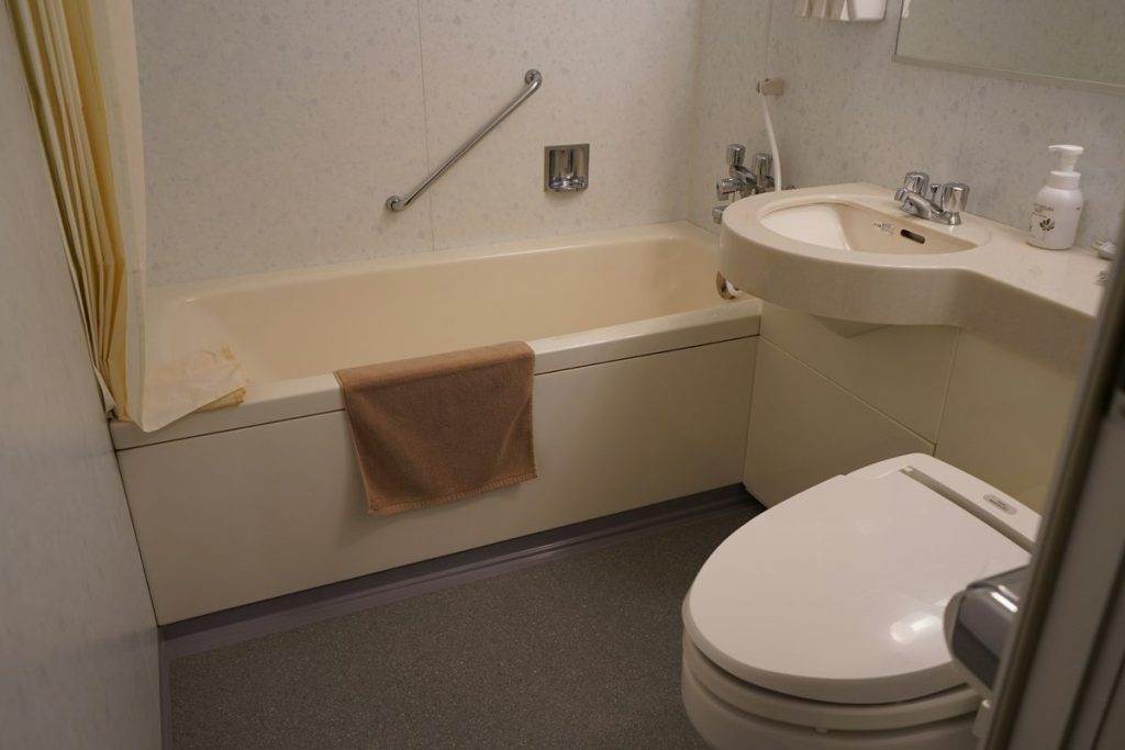 Bathtub with a diagonal grab bar on the wall beside a toilet and sink