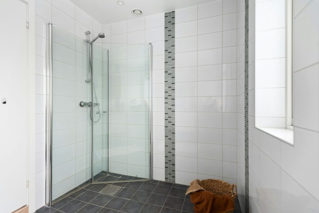 Corner walk-in shower with hinged glass doors and a handheld shower on a slide bar