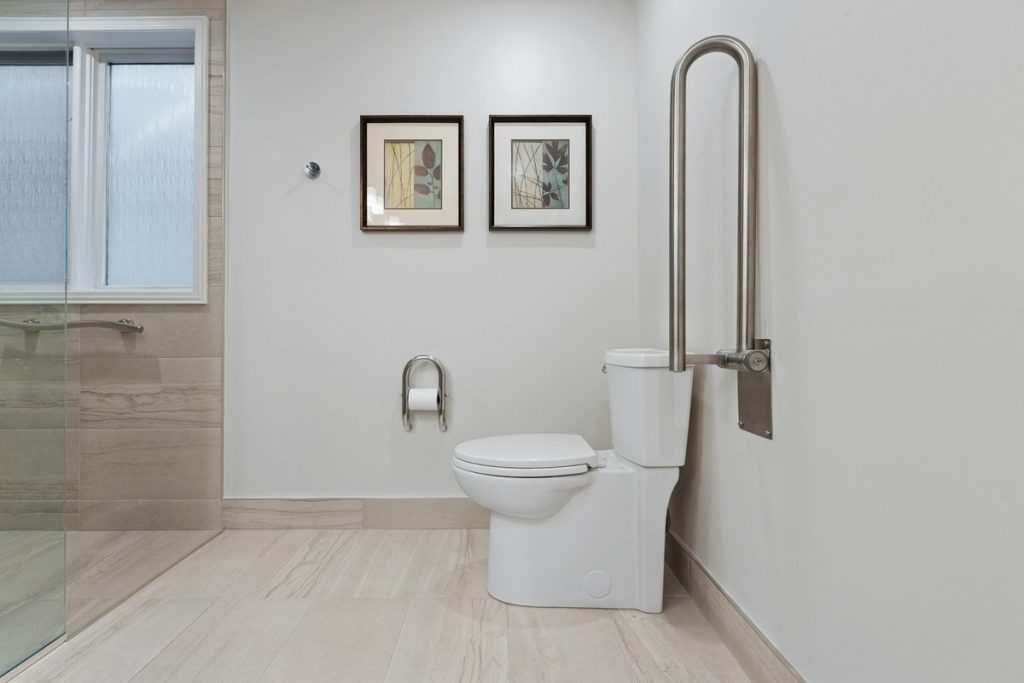 Bathroom with a fold-down grab bar beside the toilet and a glass walk-in shower
