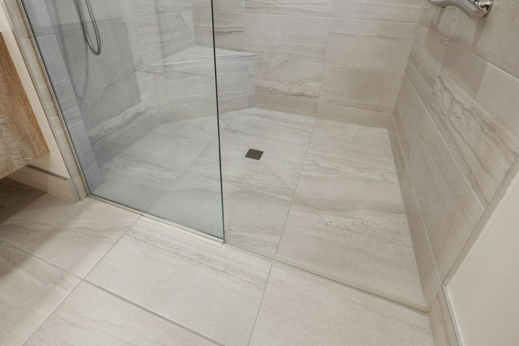 Curbless shower with a glass panel, large floor tiles and a center drain