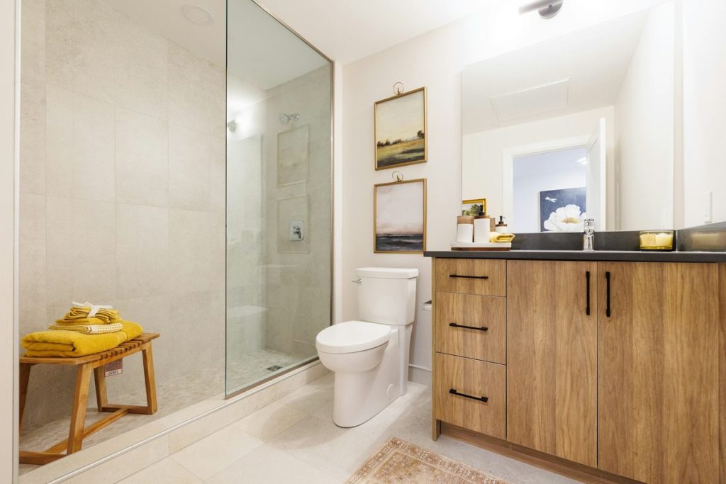 Glass walk-in shower with a freestanding wooden bench holding towels beside it