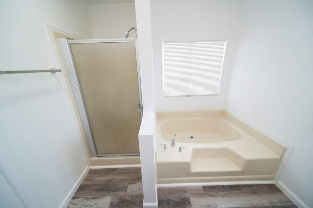 Older corner garden tub with a built-in step beside a framed shower door