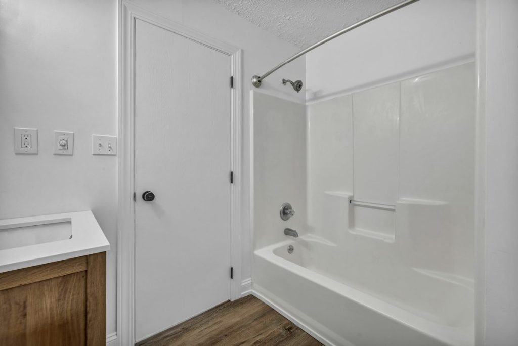 One-piece white tub and shower surround with molded shelves and a grab bar