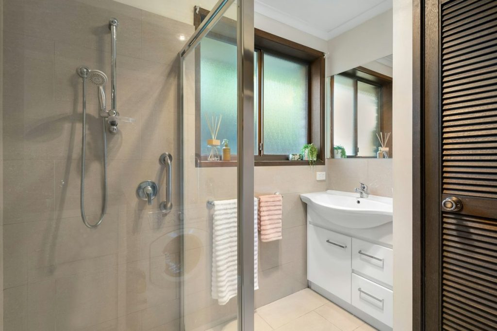Walk-in shower with a vertical grab bar beside the controls and a handheld shower on a slide bar