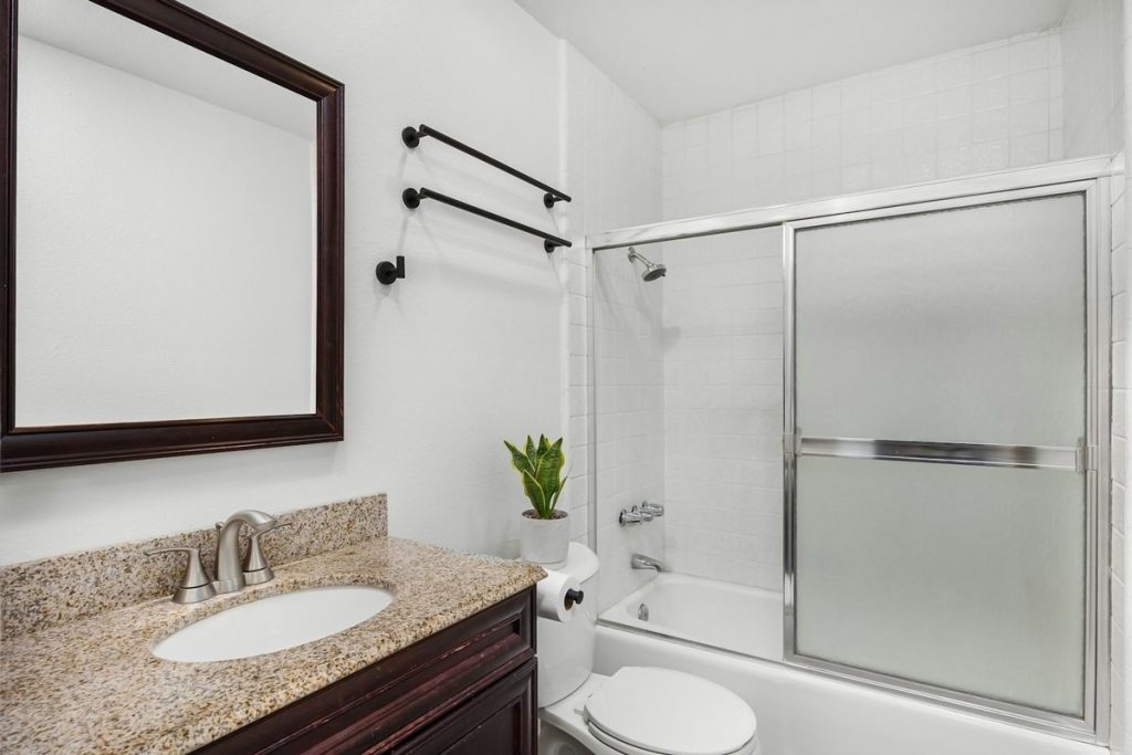 Older tub and shower with frosted sliding doors next to a granite vanity