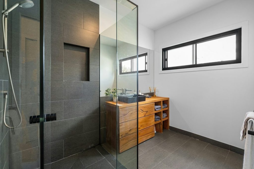 Walk-in shower with dark wall tile, a glass panel and a handheld shower