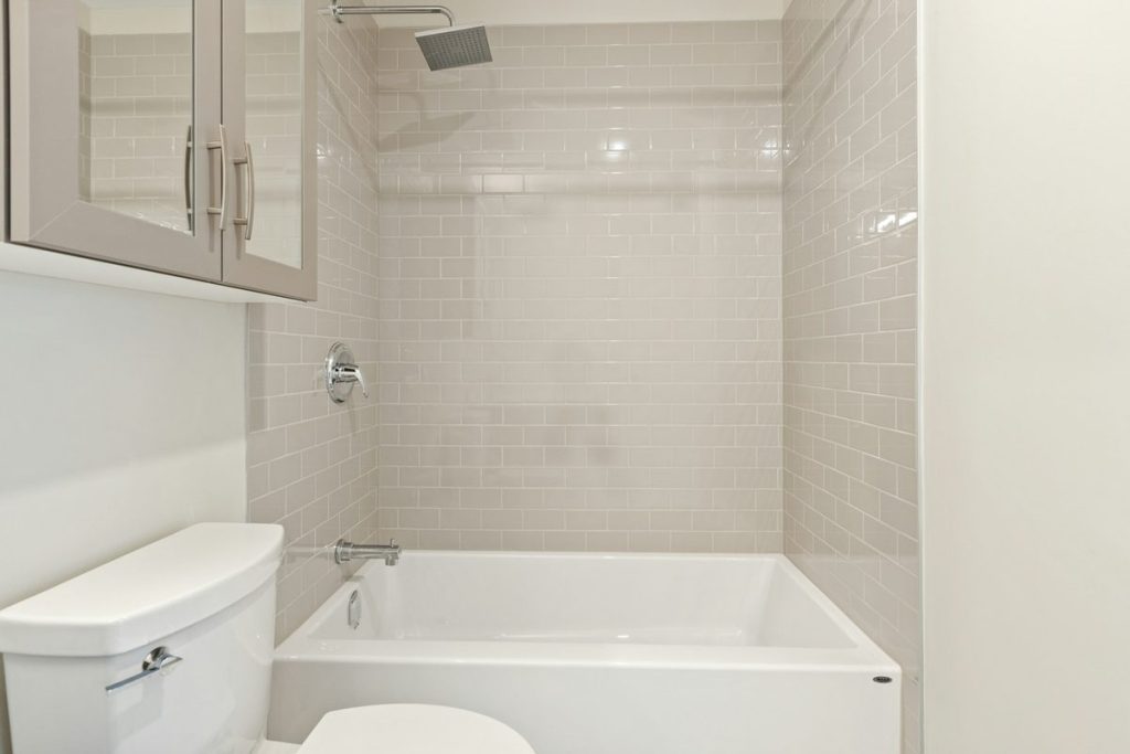 Standard alcove bathtub with subway tile walls and a shower head