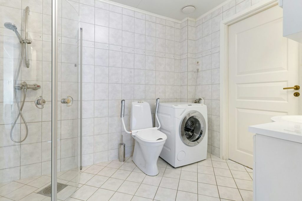 Toilet with safety rails on both sides next to a level-entry shower with a glass door