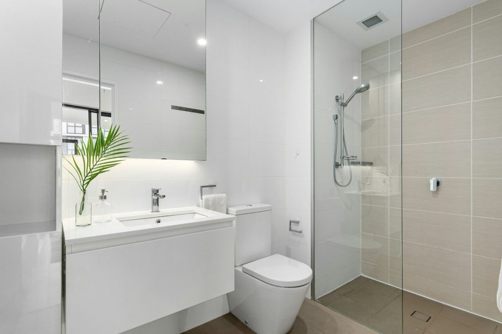 Walk-in shower with a fixed glass panel beside the toilet and vanity